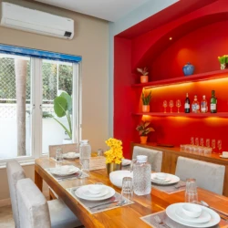 Celeste - Vio Stays - 3BHK Luxury Private Pool Villas In Baga - dining room with dining table and chairs, plates, fan & glasses. On the side - flower pots, paintings, wine glasses, tea cups, & air conditioner