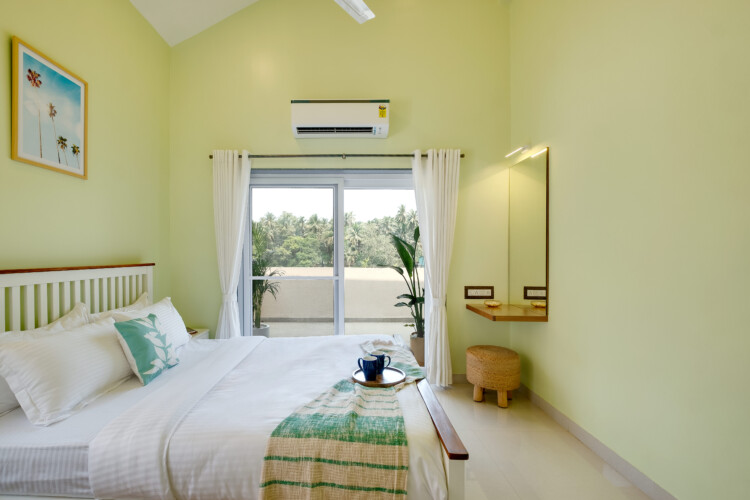 Ina - Villa in Siolim Goa - bedroom 3 of 4 - paintings, attached washroom, balcony with paddy field view, side table, mirror and dressing table, well light bedrooom